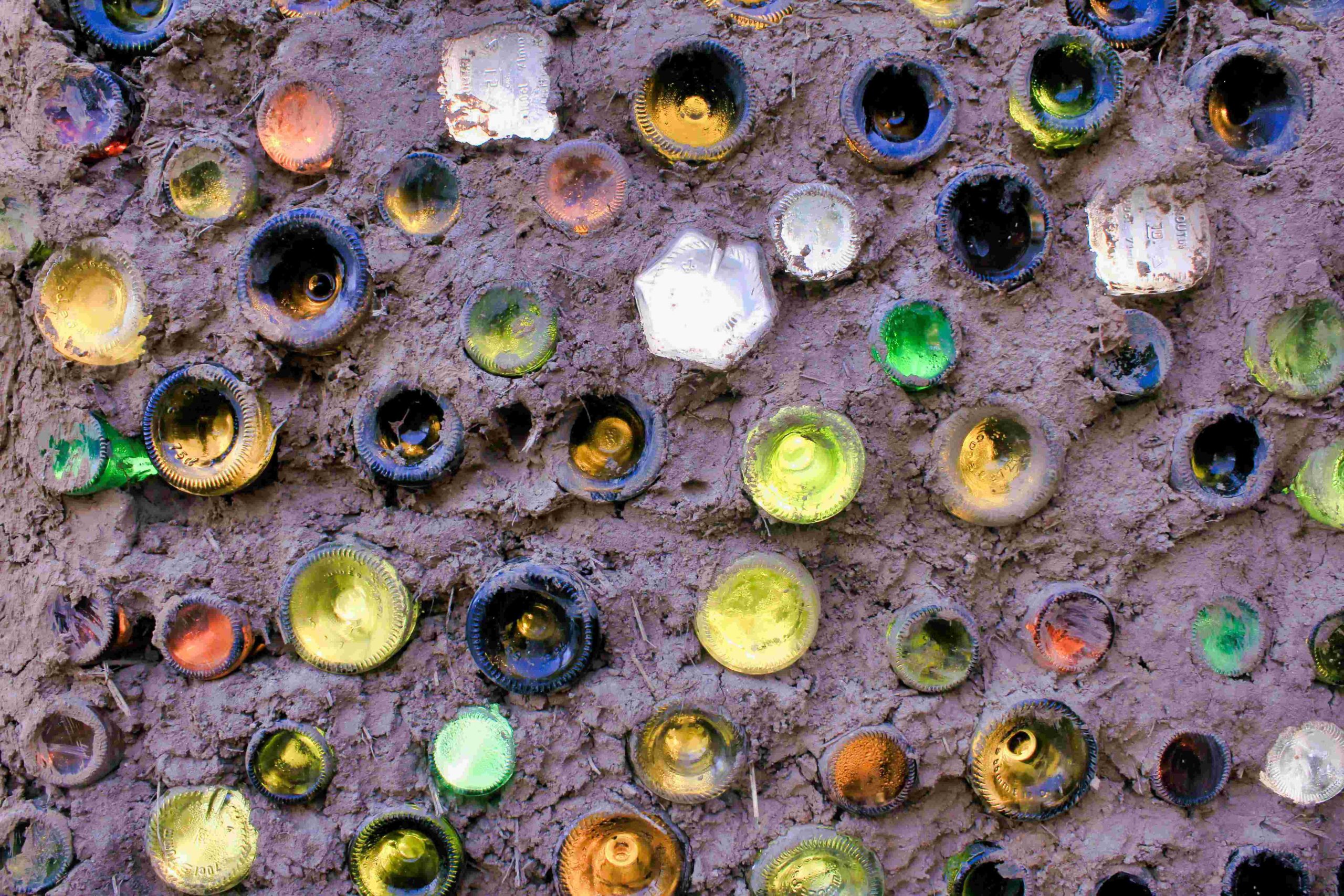 un mur en bouteilles de verre fait maison avec des bouteilles de récupération de plusieurs couleurs et tailles